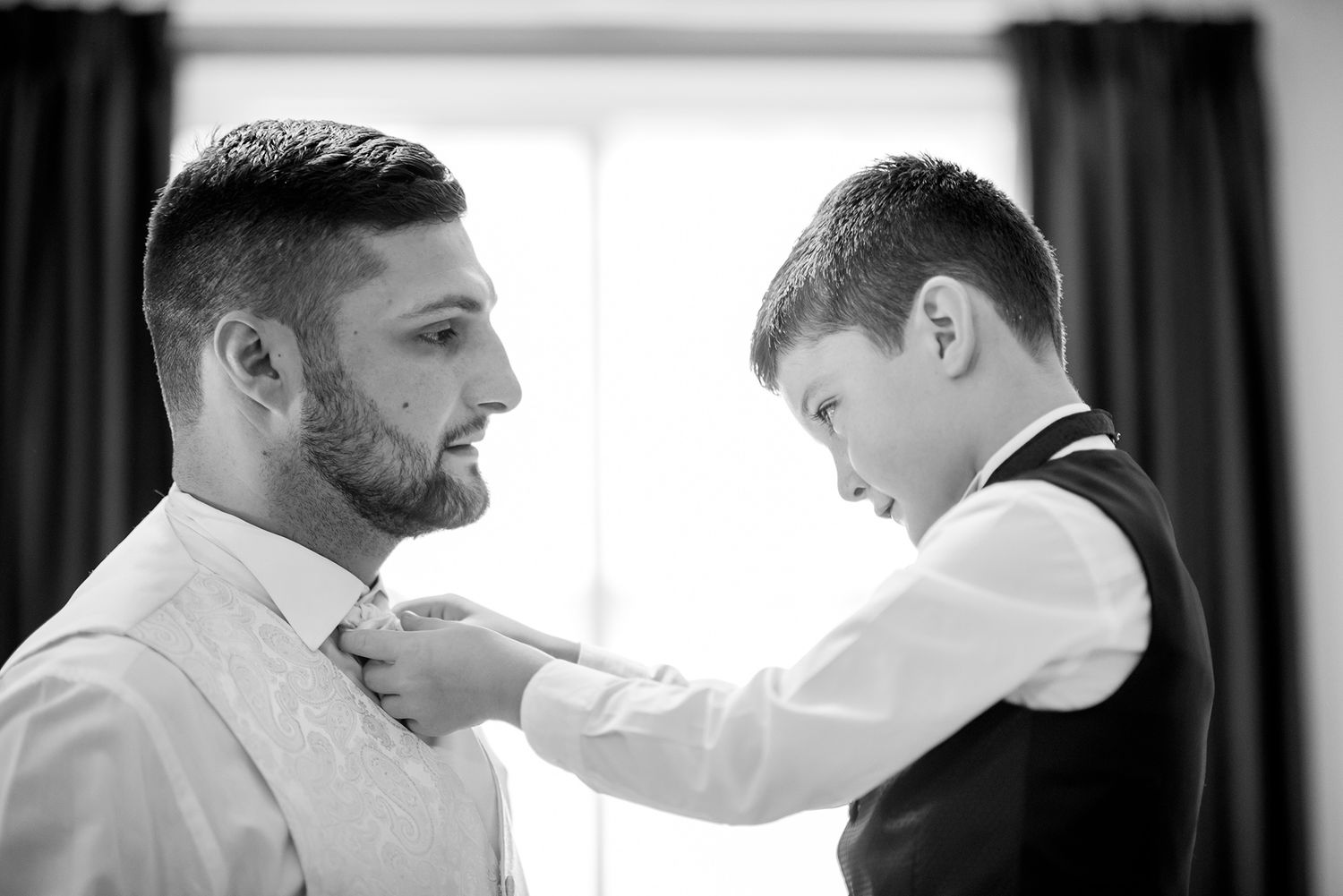 An intimate black and white photo capturing a moment of dress preparation near a window.