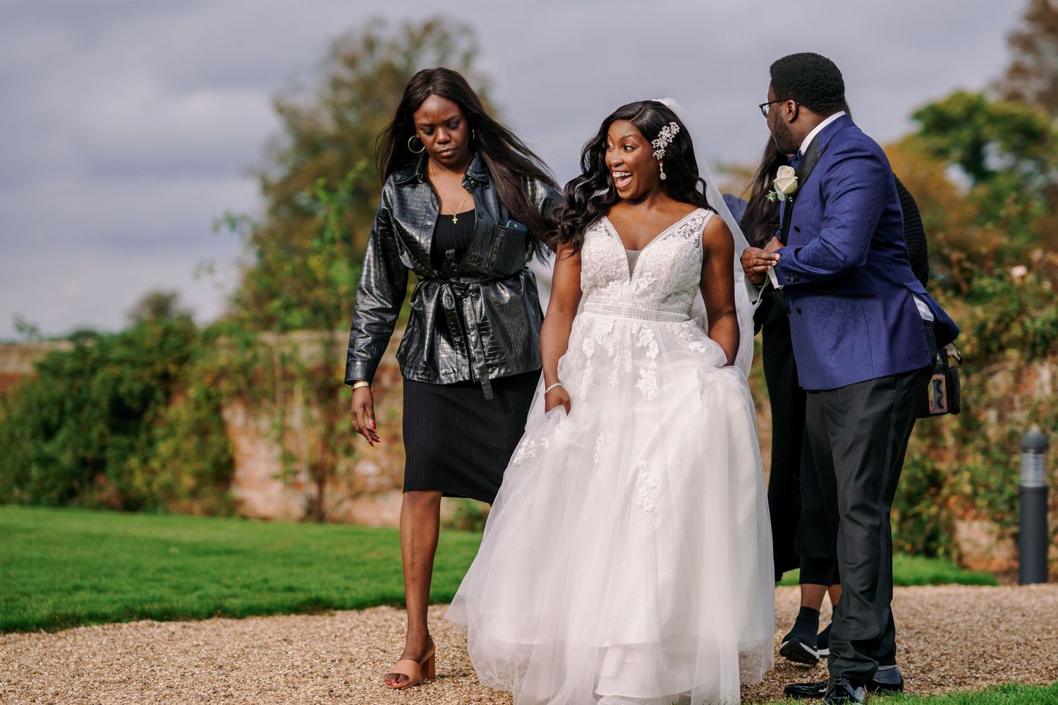 Wedding party in formal attire walking together on a garden path during an outdoor celebration.