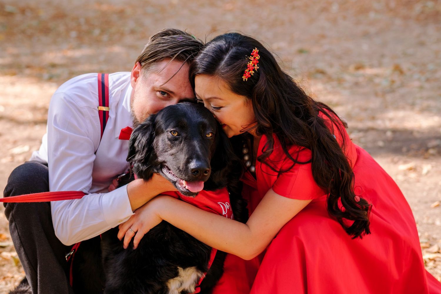 A couple in red and white outfits shares tender moments in an outdoor photo session with their small dog.