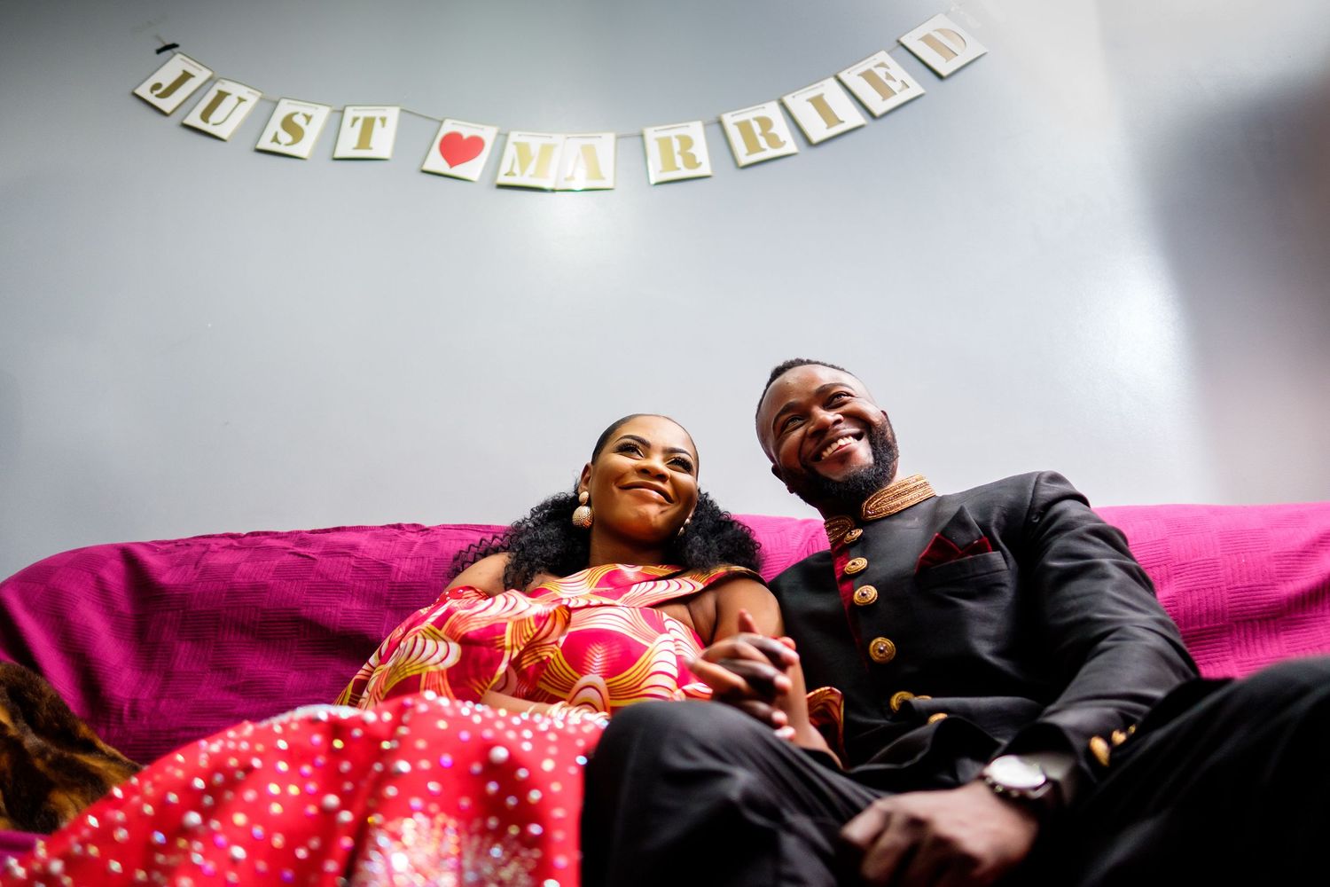 A couple relaxing on pink bedding under decorative banner letters on the wall.