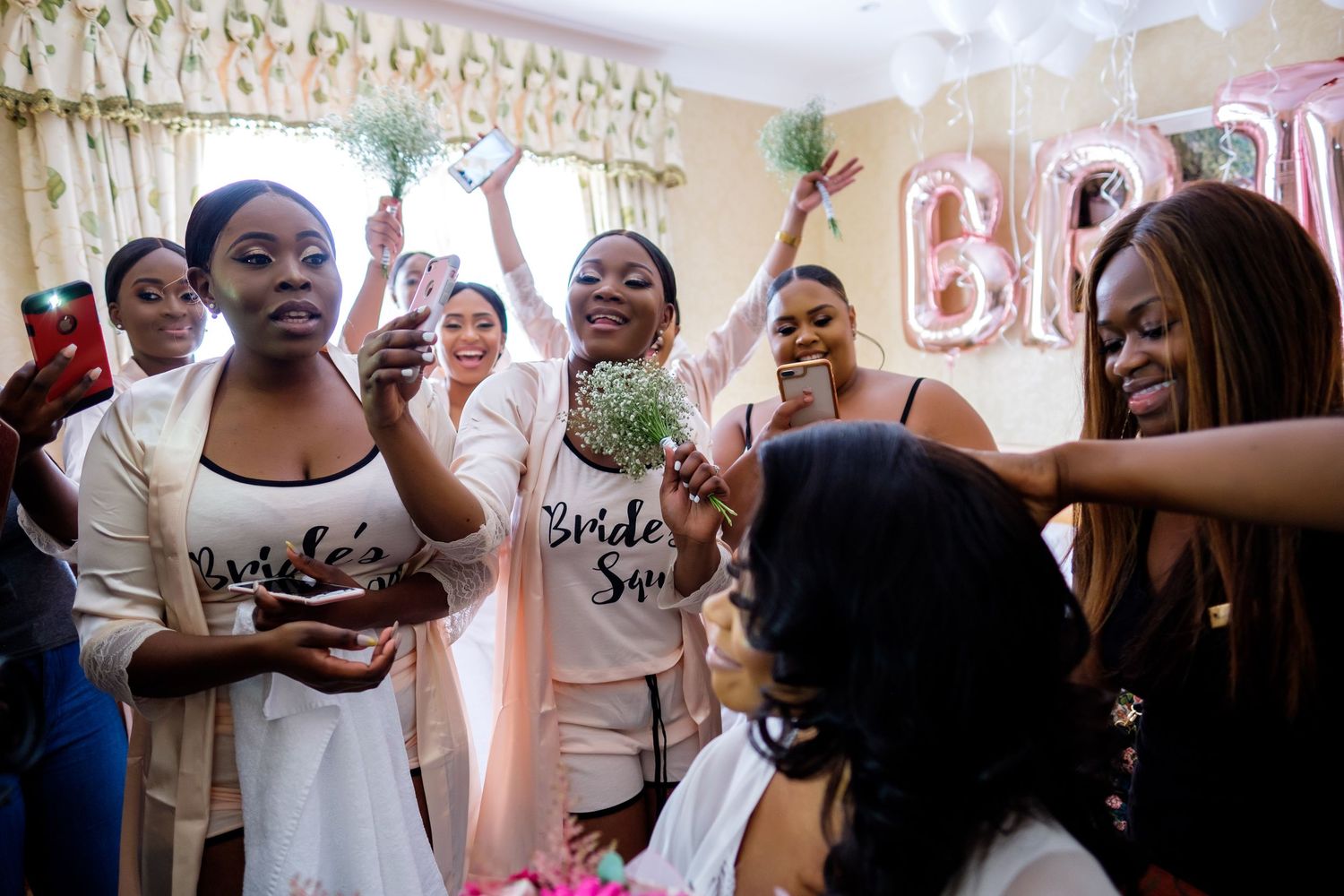 Wedding party celebrates joyfully in matching robes with celebratory drinks and decor.