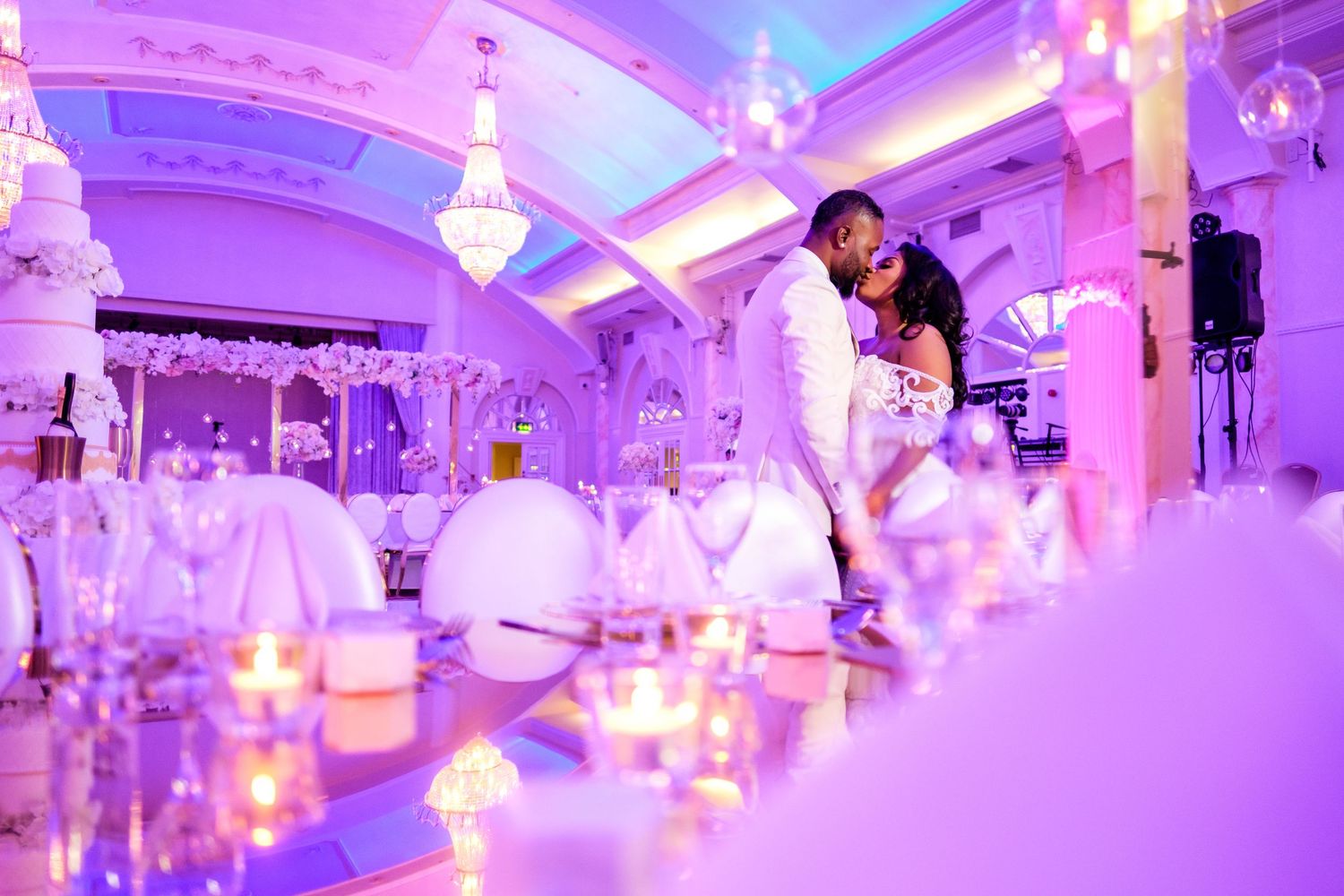 Luxurious ballroom decorated in purple lighting with crystal chandeliers and white chairs.
