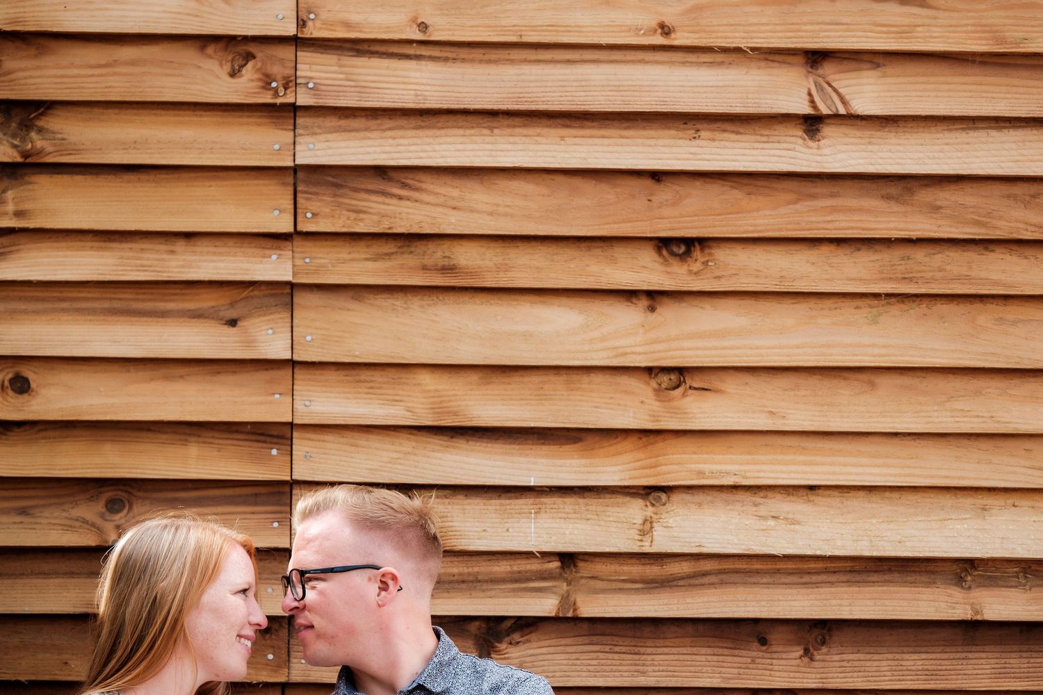 Couple poses against rustic wooden wall backdrop during outdoor photoshoot.