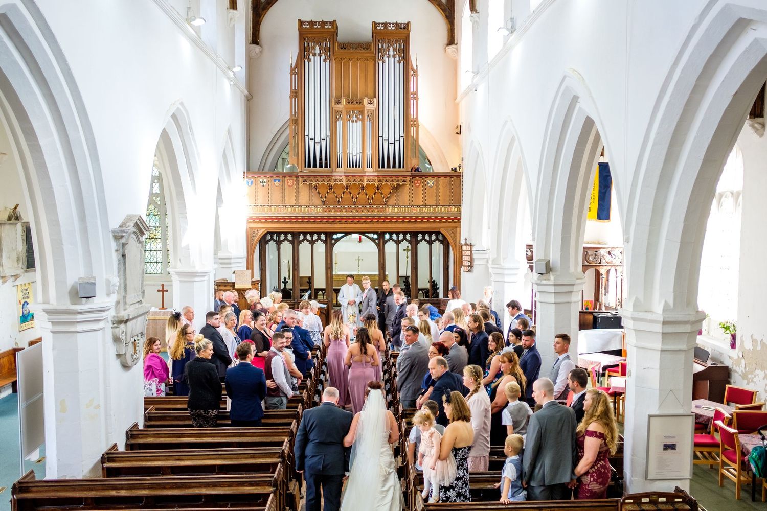 A church wedding ceremony with guests seated in wooden pews beneath a grand pipe organ.