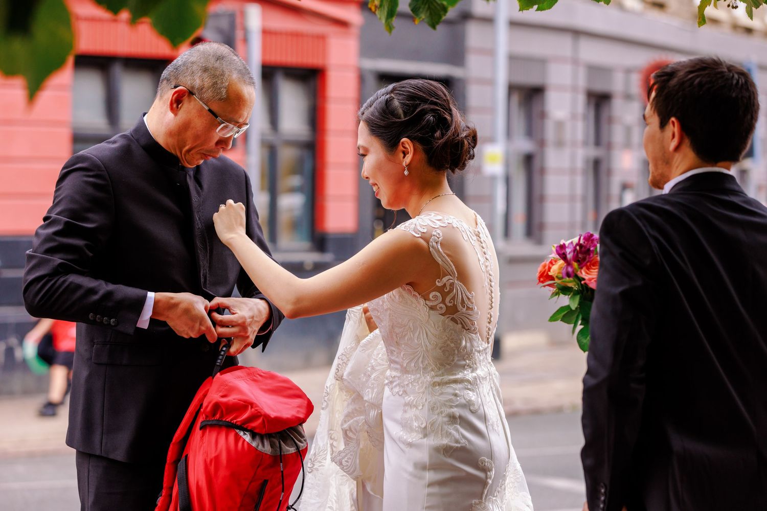 A couple in wedding attire interacts on a city street while another person looks on.