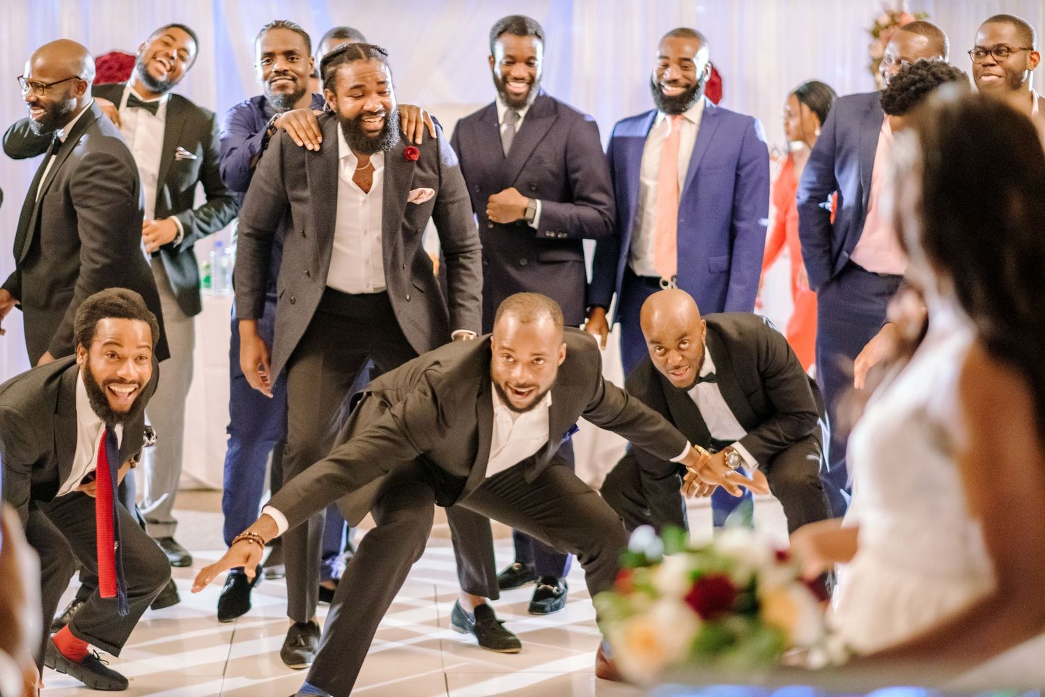 Wedding party members perform synchronized dance moves in formal attire during reception celebration.