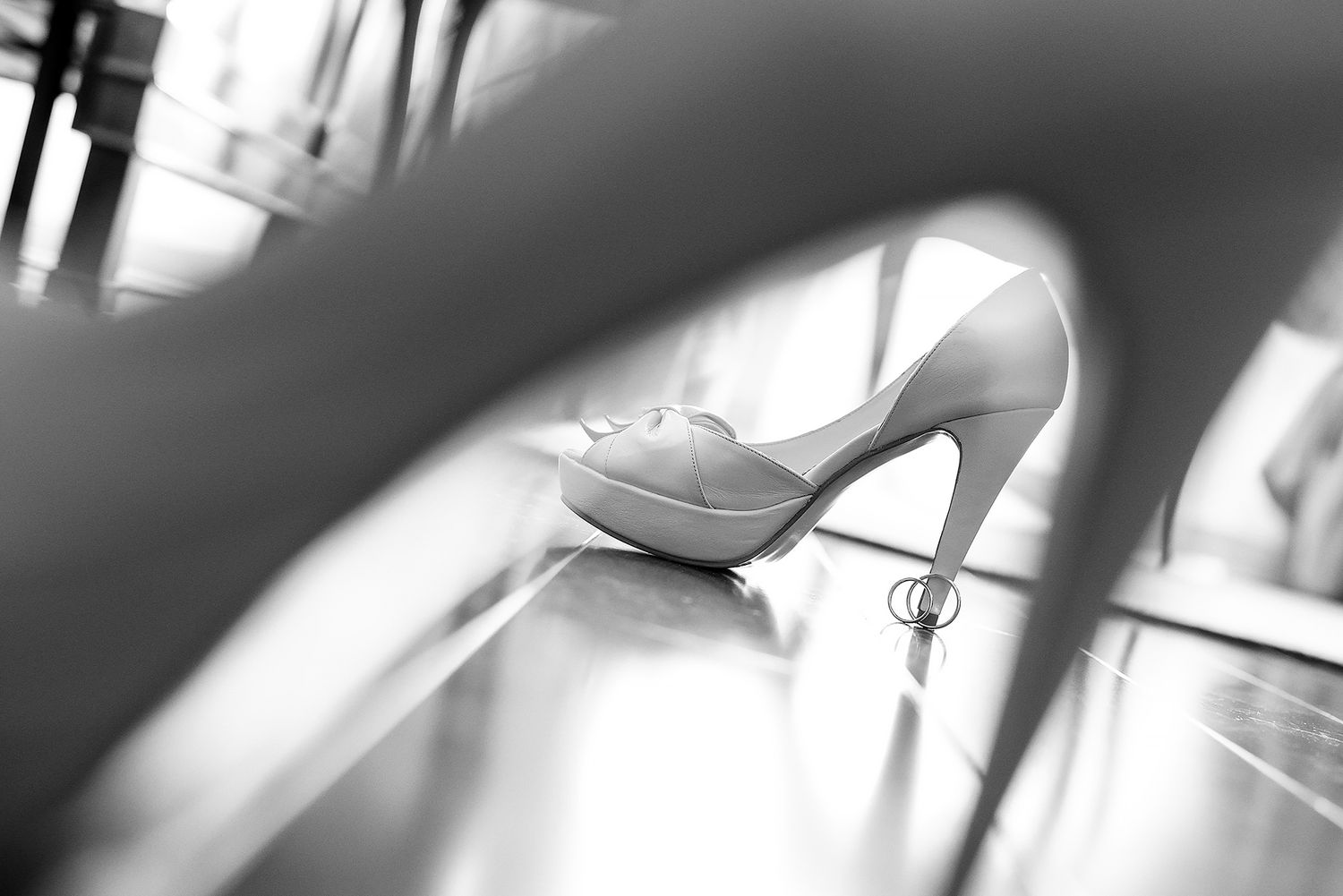 Artistic detail shot of a white bridal shoe through blurred foreground.