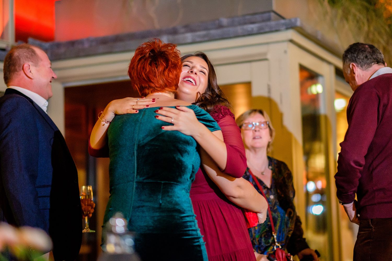 People embracing and laughing together at an evening celebration.