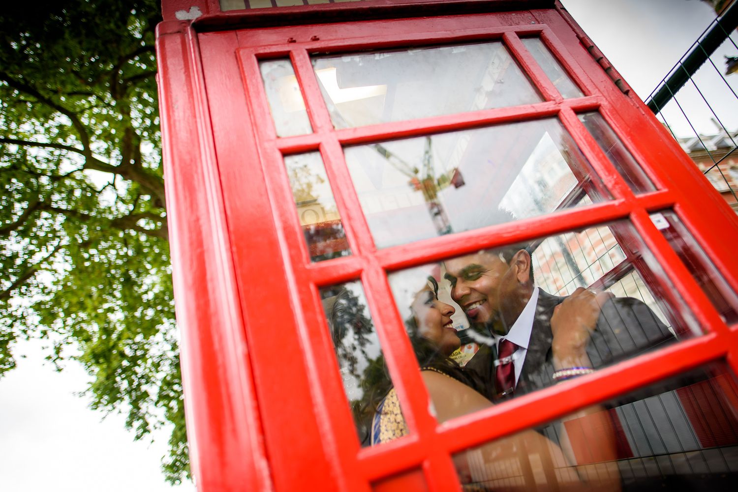 Creative shots through red telephone booth frames capturing romantic moments.