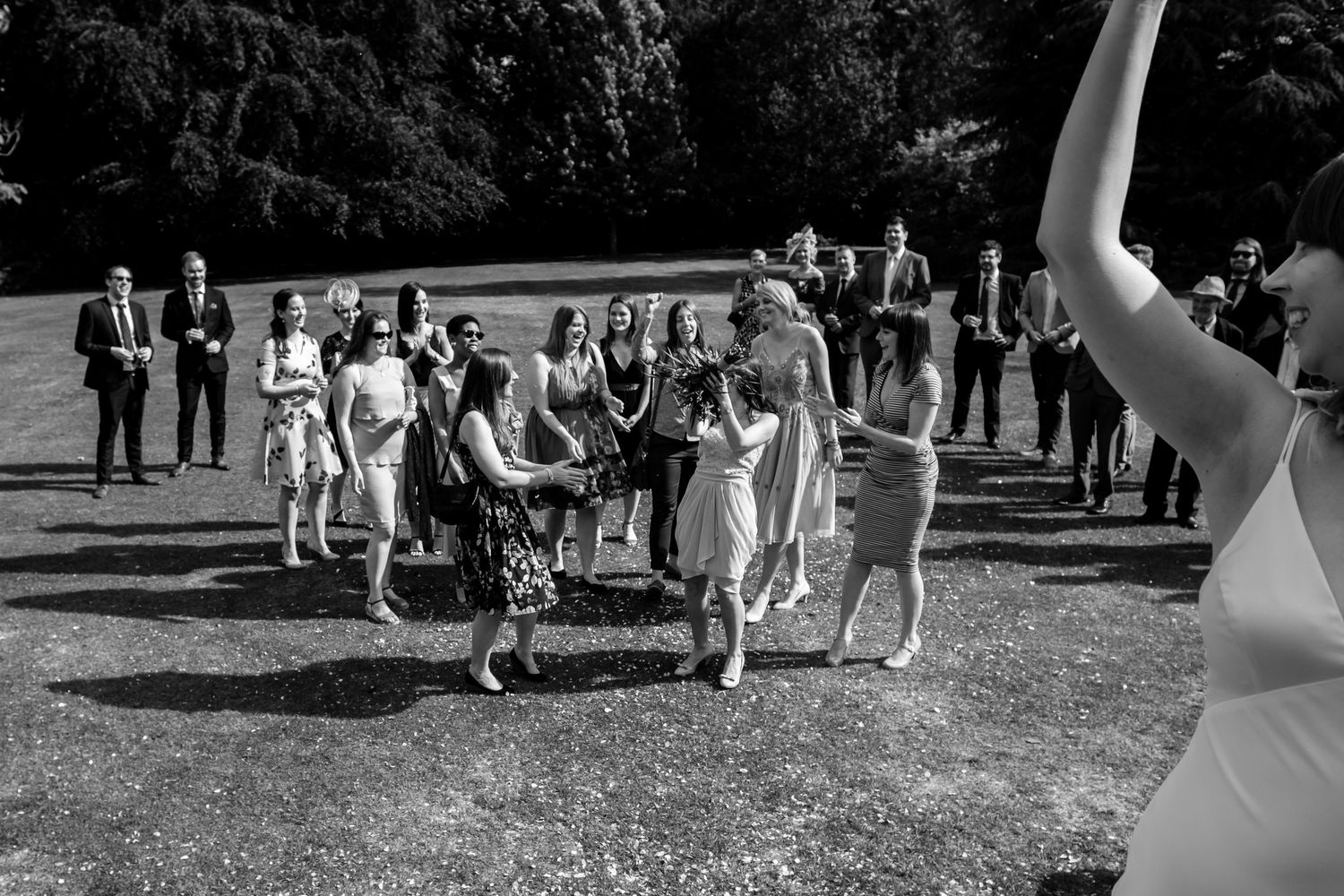 Wedding party and guests stand together on a manicured lawn for group photos.