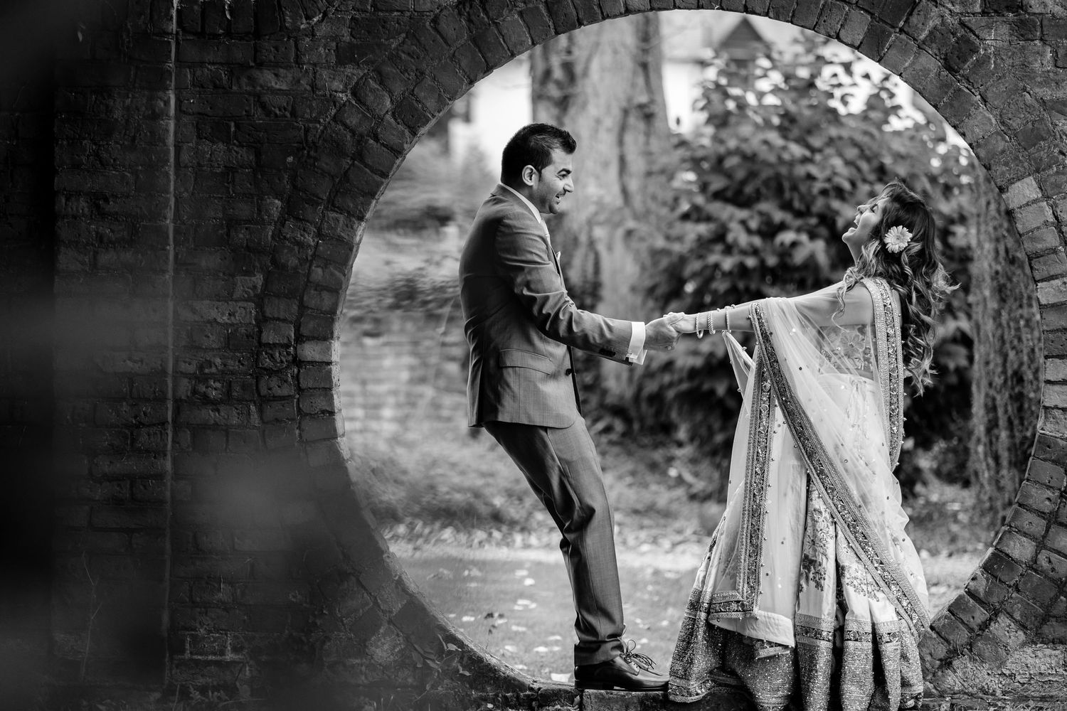 Black and white romantic photoshoot showing playful moments near a brick wall.