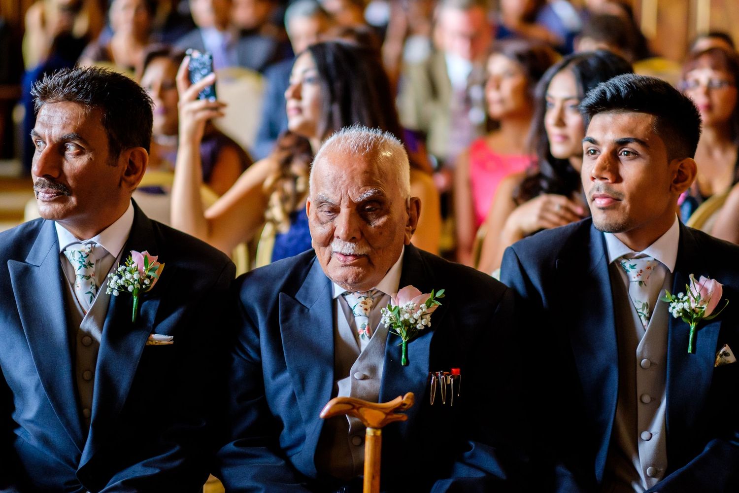 Groomsmen in navy suits with floral boutonnieres smile during an elegant wedding ceremony.