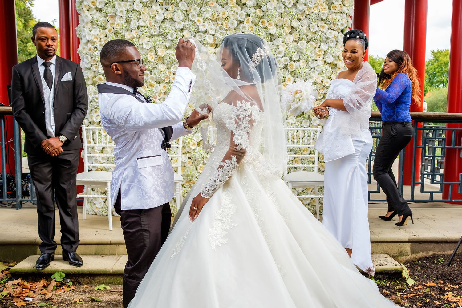 Elegant wedding ceremony setup with white floral wall and red architectural details.