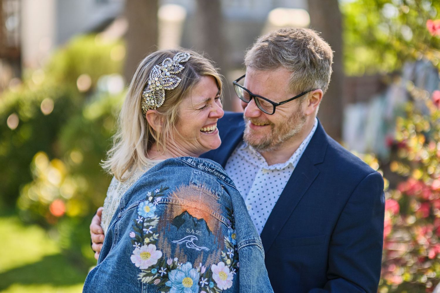 Couple shares intimate moment in garden setting with blue denim jacket and navy suit.