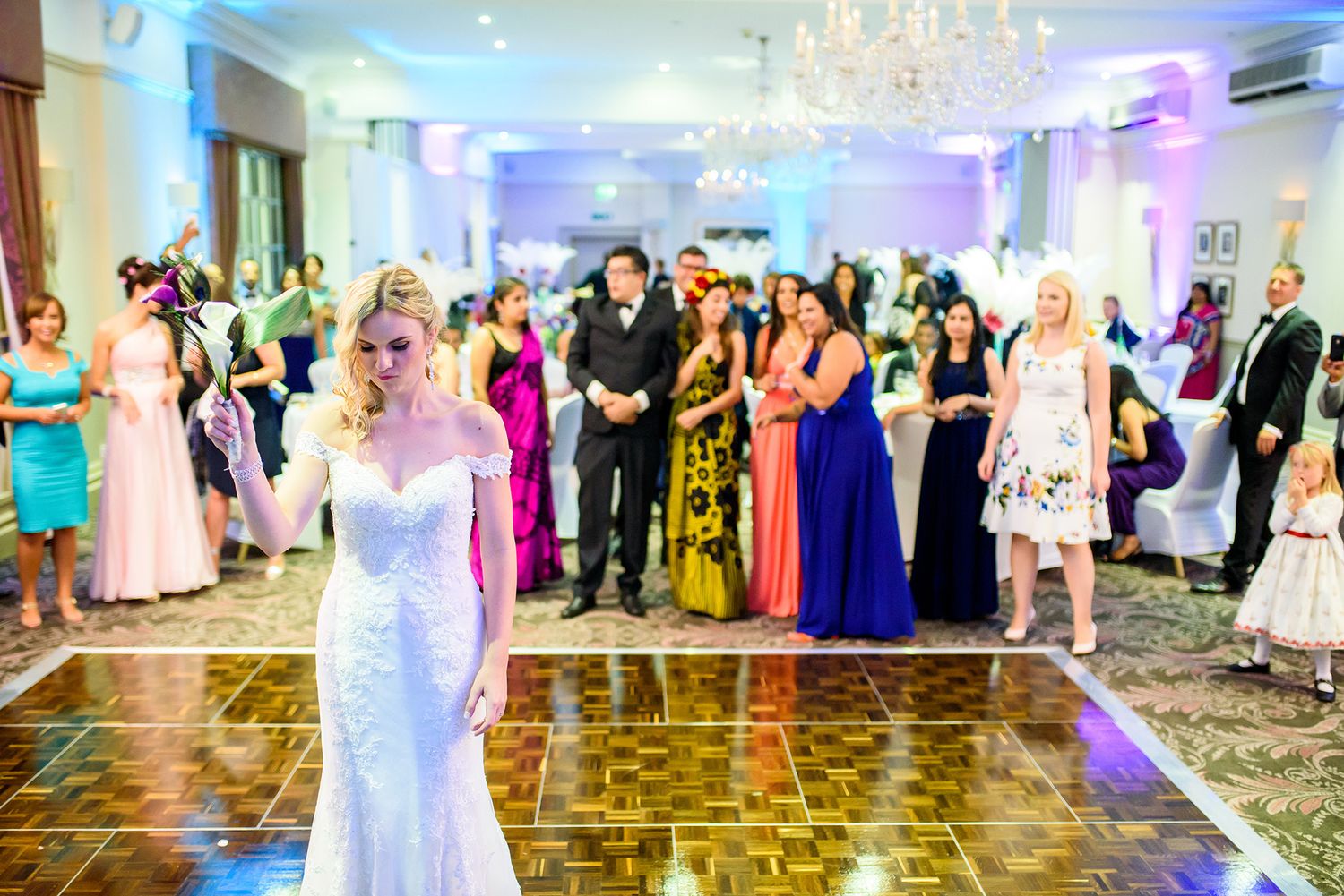 Elegant ballroom decorated for a wedding reception with crystal chandeliers and colorful uplighting.
