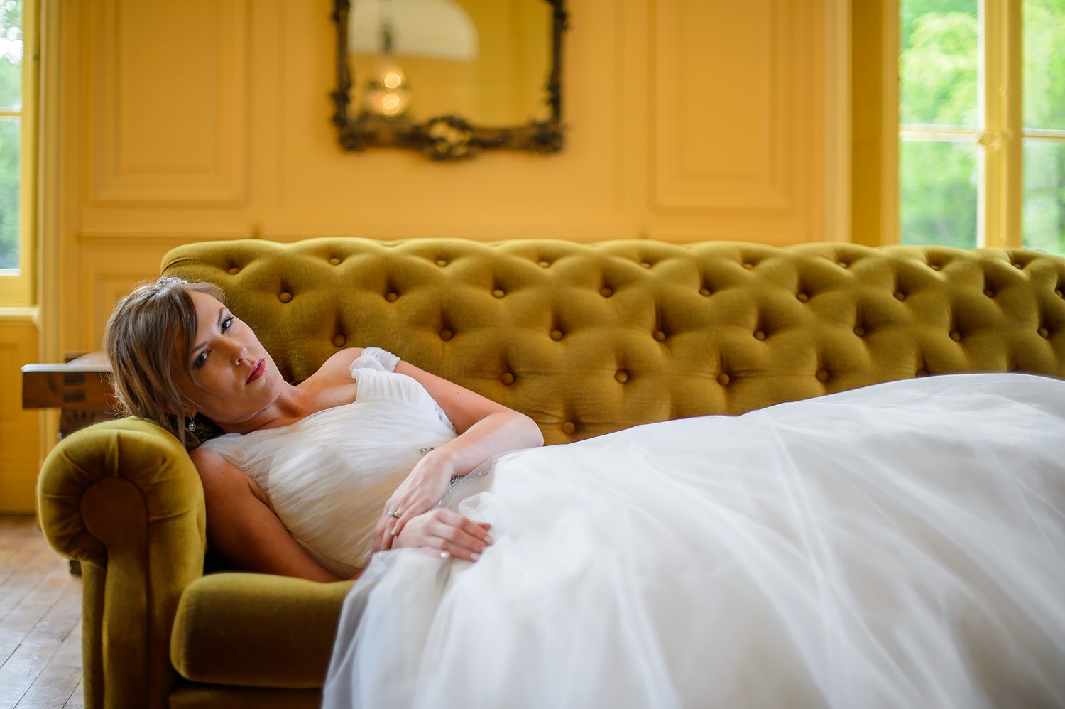 A formal reception area with elegant yellow walls, ornate gold framed mirrors, and luxurious cream-colored sofas.