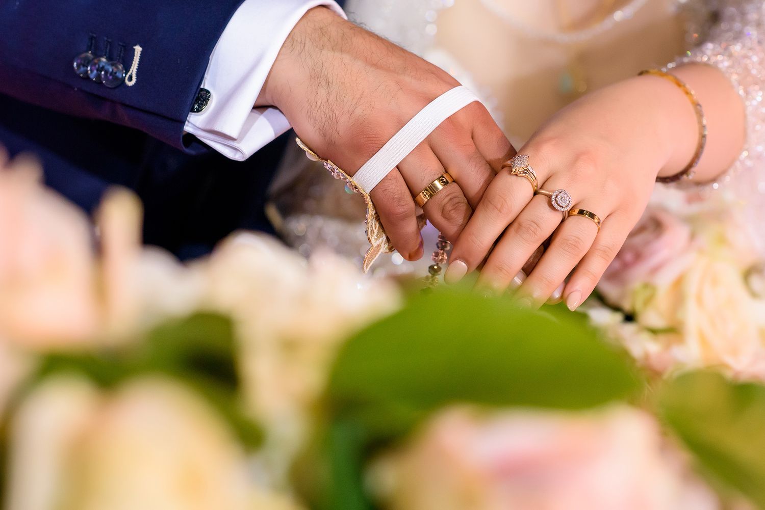 Close-up of hands with wedding rings against a soft pink floral background.