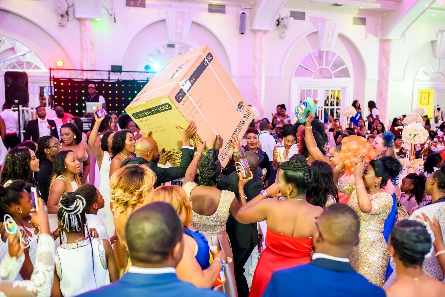 Energetic wedding party crowd dancing under colorful lights in an ornate ballroom.