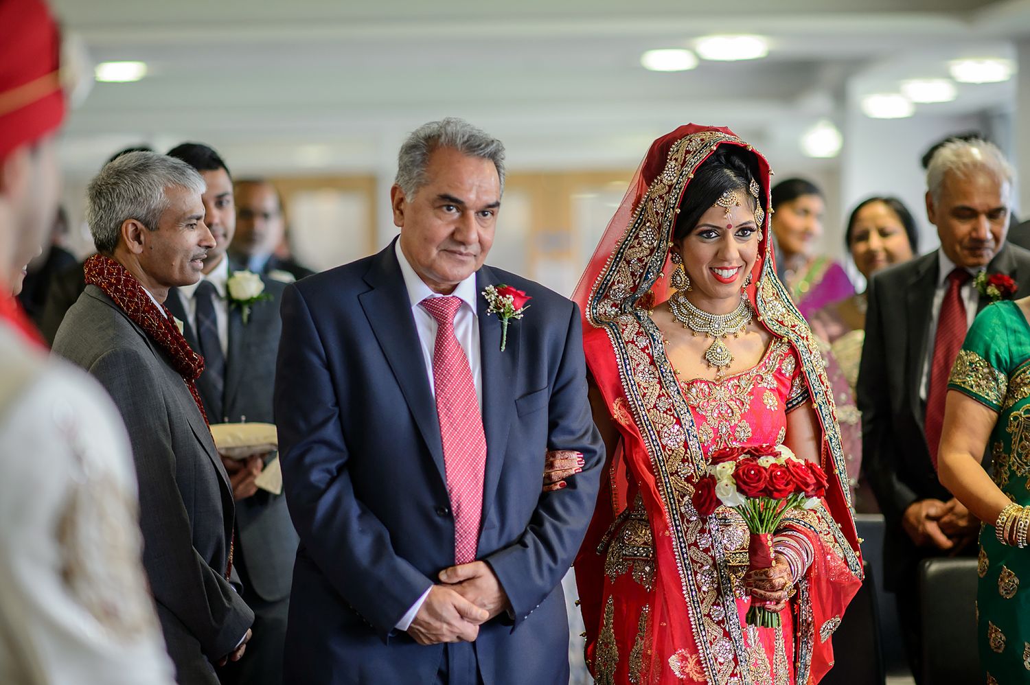 Wedding ceremony attendees in formal wear and traditional Indian clothing at indoor venue.