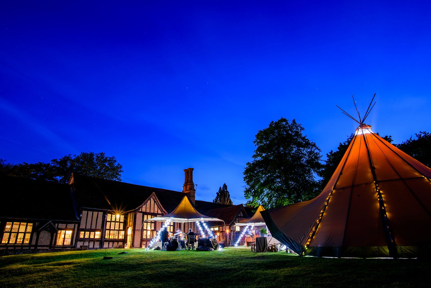 Illuminated teepee-style tents glow against deep blue twilight sky.