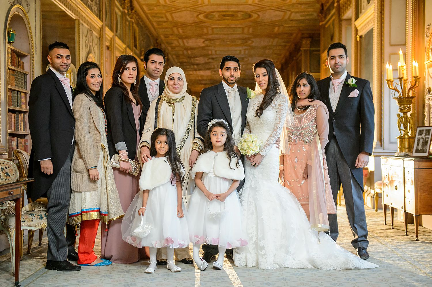 Full wedding party portrait in formal attire standing in a grand hallway with ornate details.