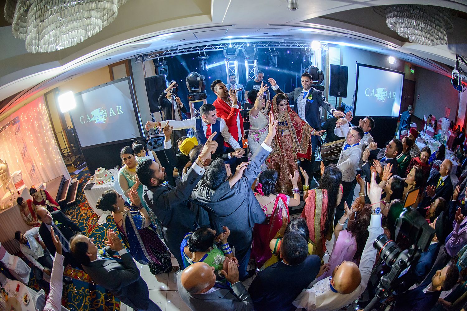 Wide-angle view of a packed wedding reception hall with chandelier and party lighting.