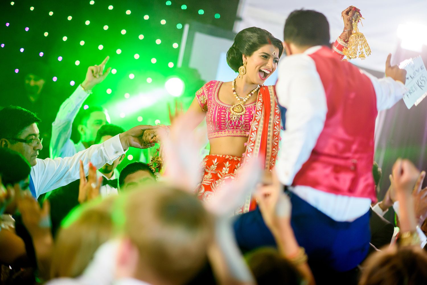 Green lighting bathes a crowded dance floor as guests celebrate at an Indian wedding reception.