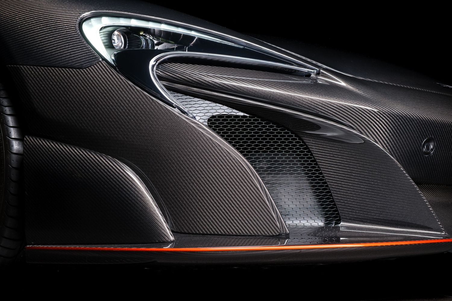 Close-up detail shot of a McLaren's sleek carbon fiber bodywork with orange accents in dramatic lighting.