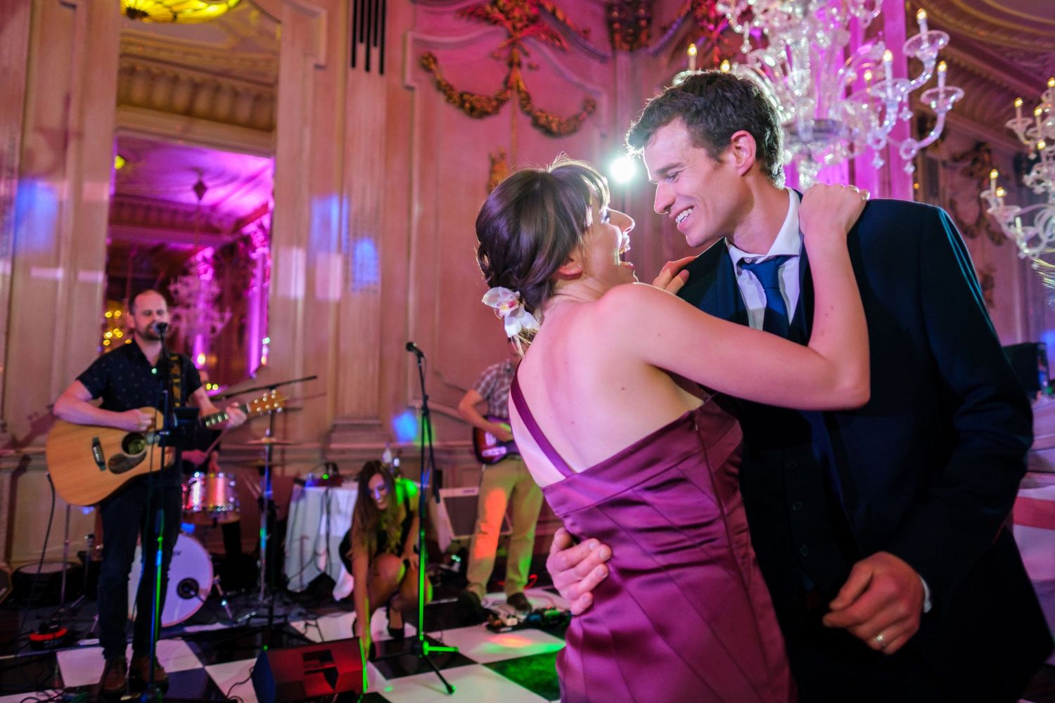 Wedding guests dancing and celebrating on a purple-lit dance floor at an elegant reception venue.