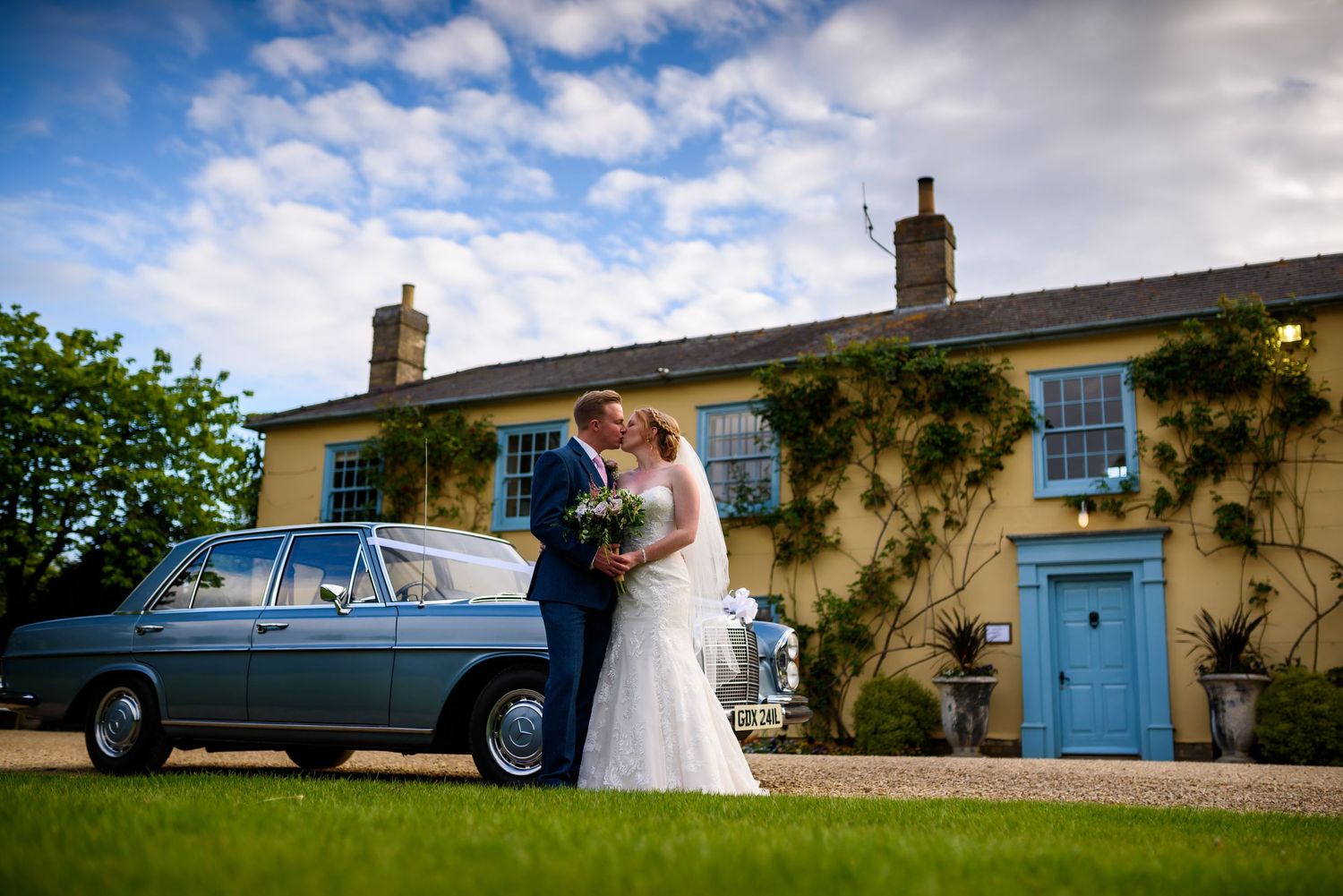 Classic blue vintage car parked outside a countryside venue with white walls and blue door.