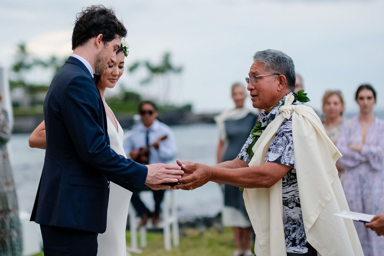 Traditional Hawaiian wedding ceremony taking place outdoors by the ocean.