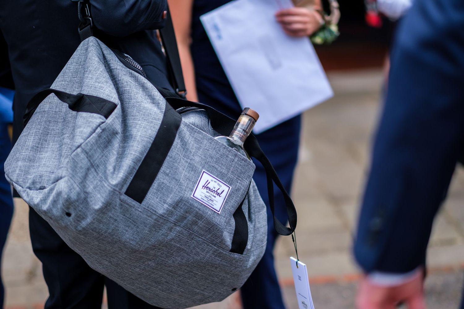 Students wearing backpacks walk together on a campus pathway carrying gray Herschel bags.