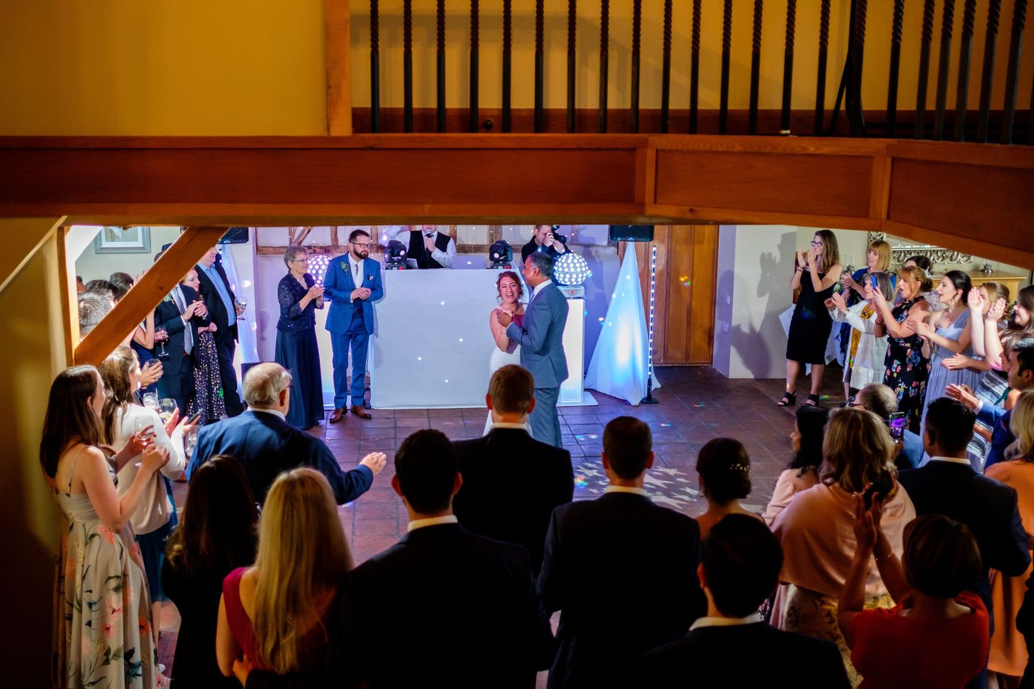 Wedding guests dance and celebrate on a crowded dance floor at an indoor reception venue.