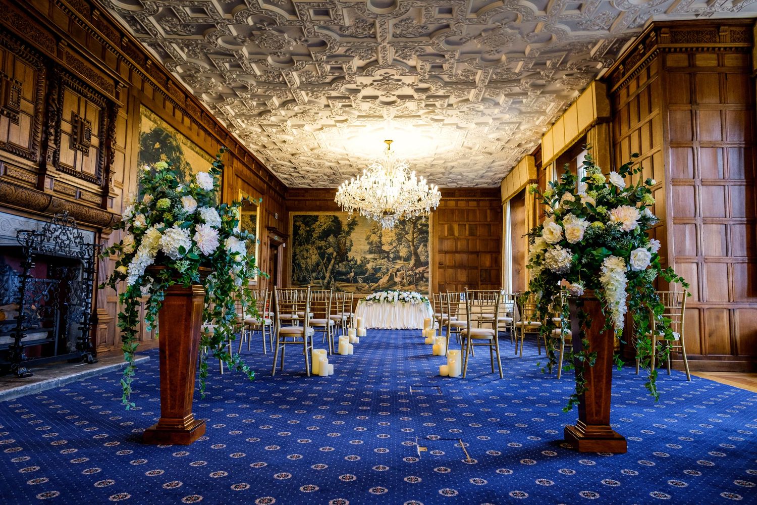 Elegant banquet hall interior with ornate chandeliers, wood paneling and blue carpeting shown in panoramic view.