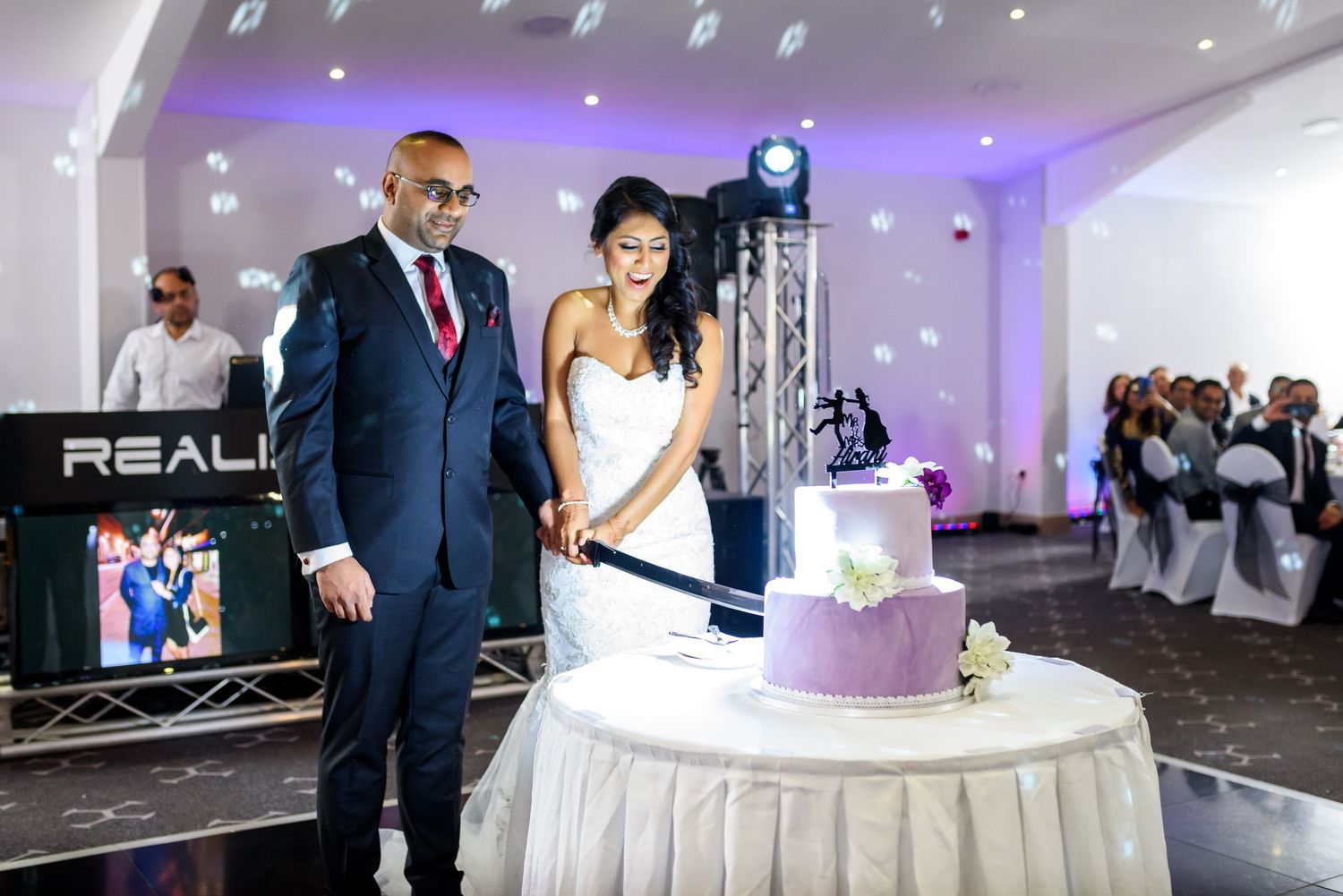 Wedding reception venue with purple uplighting, white dance floor, and elegant cake display.
