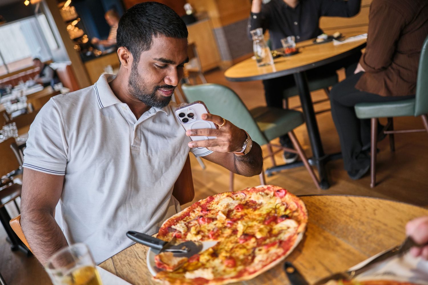 Person in white polo shirt eating a freshly baked pepperoni pizza at a restaurant.