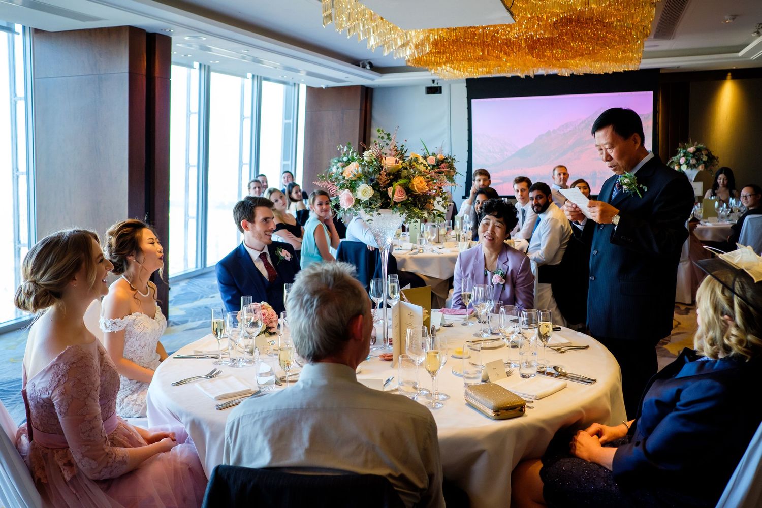 Elegant wedding reception setup with round tables and large windows overlooking the city.