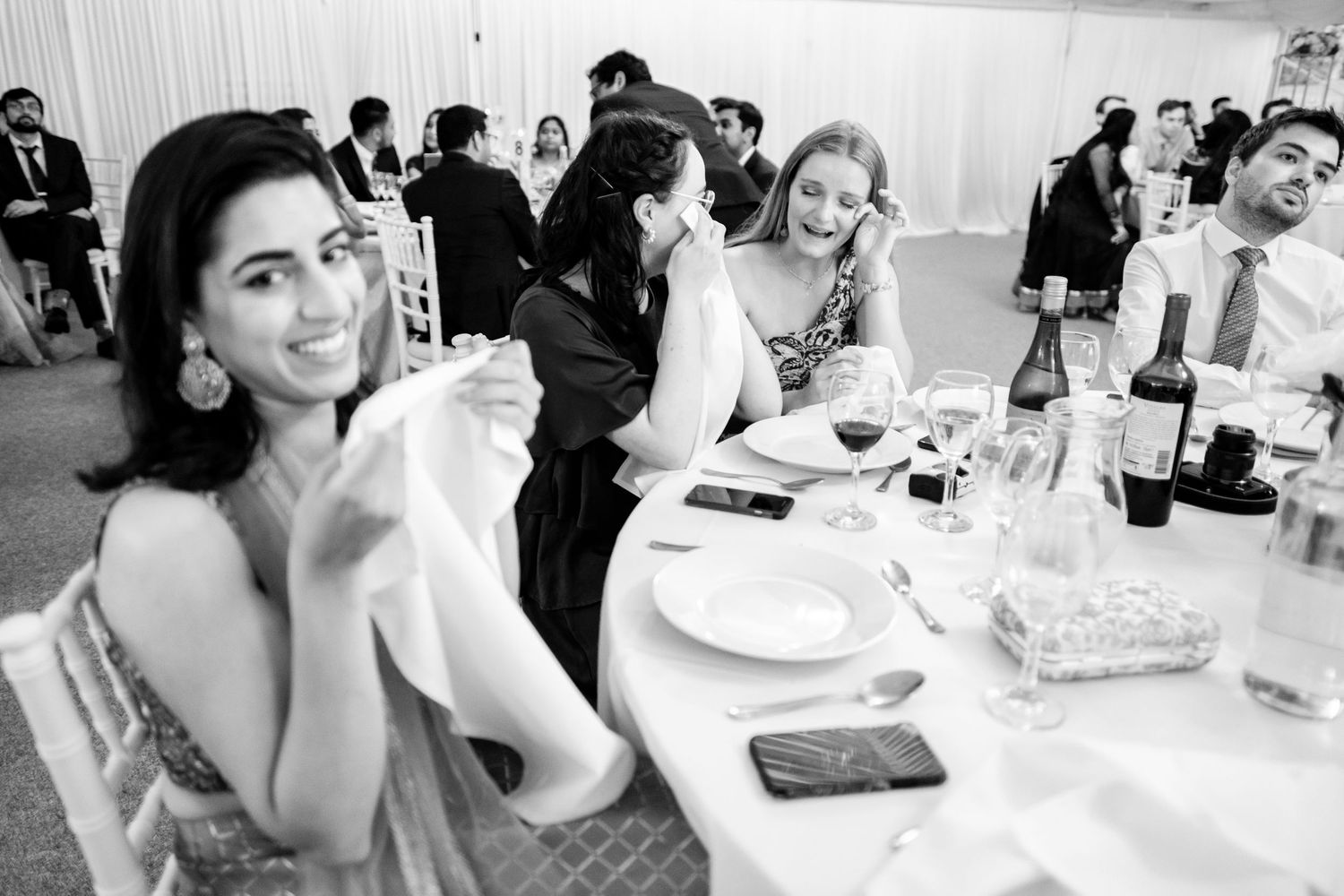 Black and white reception photo showing guests dining at tables in elegant marquee setting.