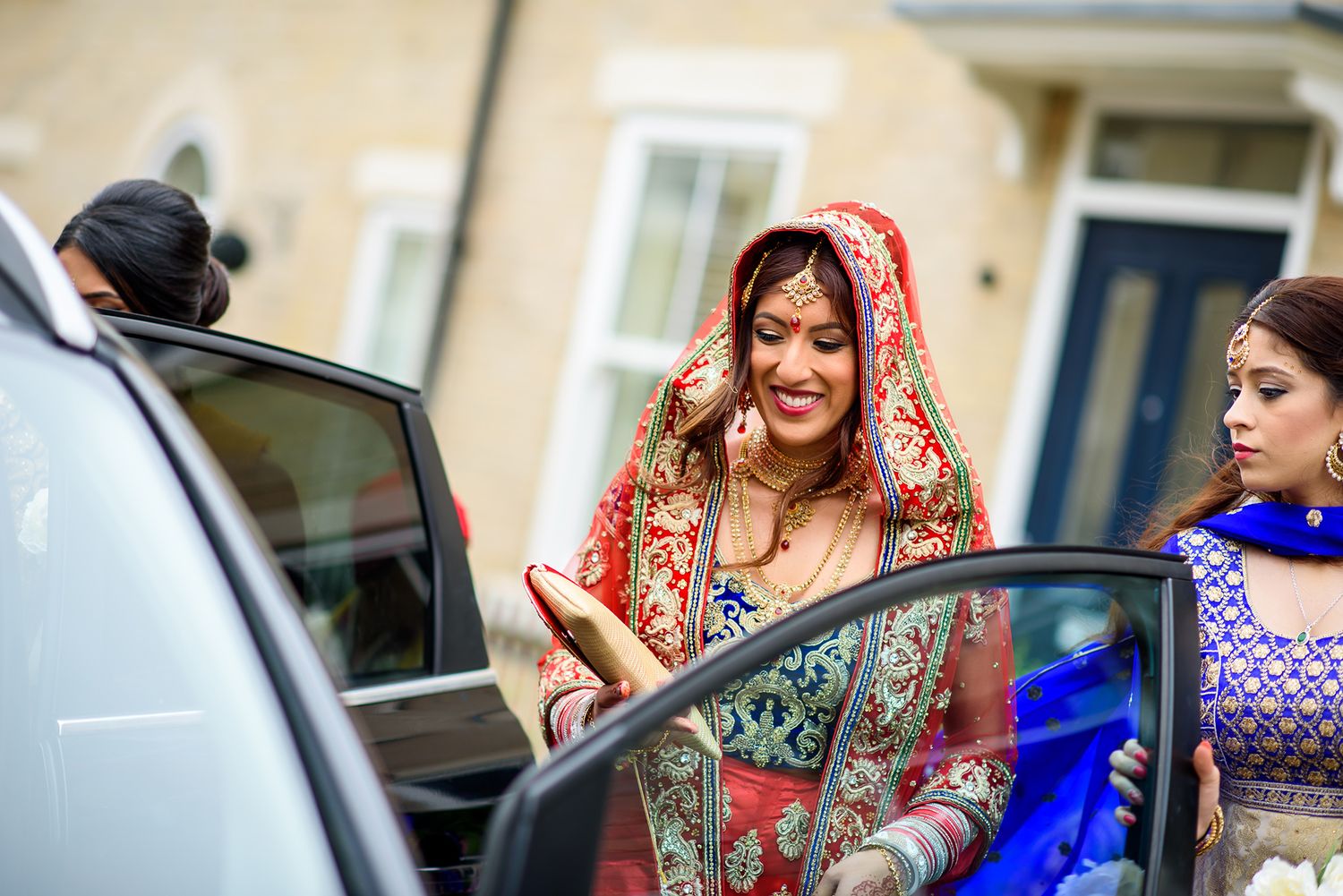 A bride in an embroidered red lehenga steps out of a car during her wedding celebration.