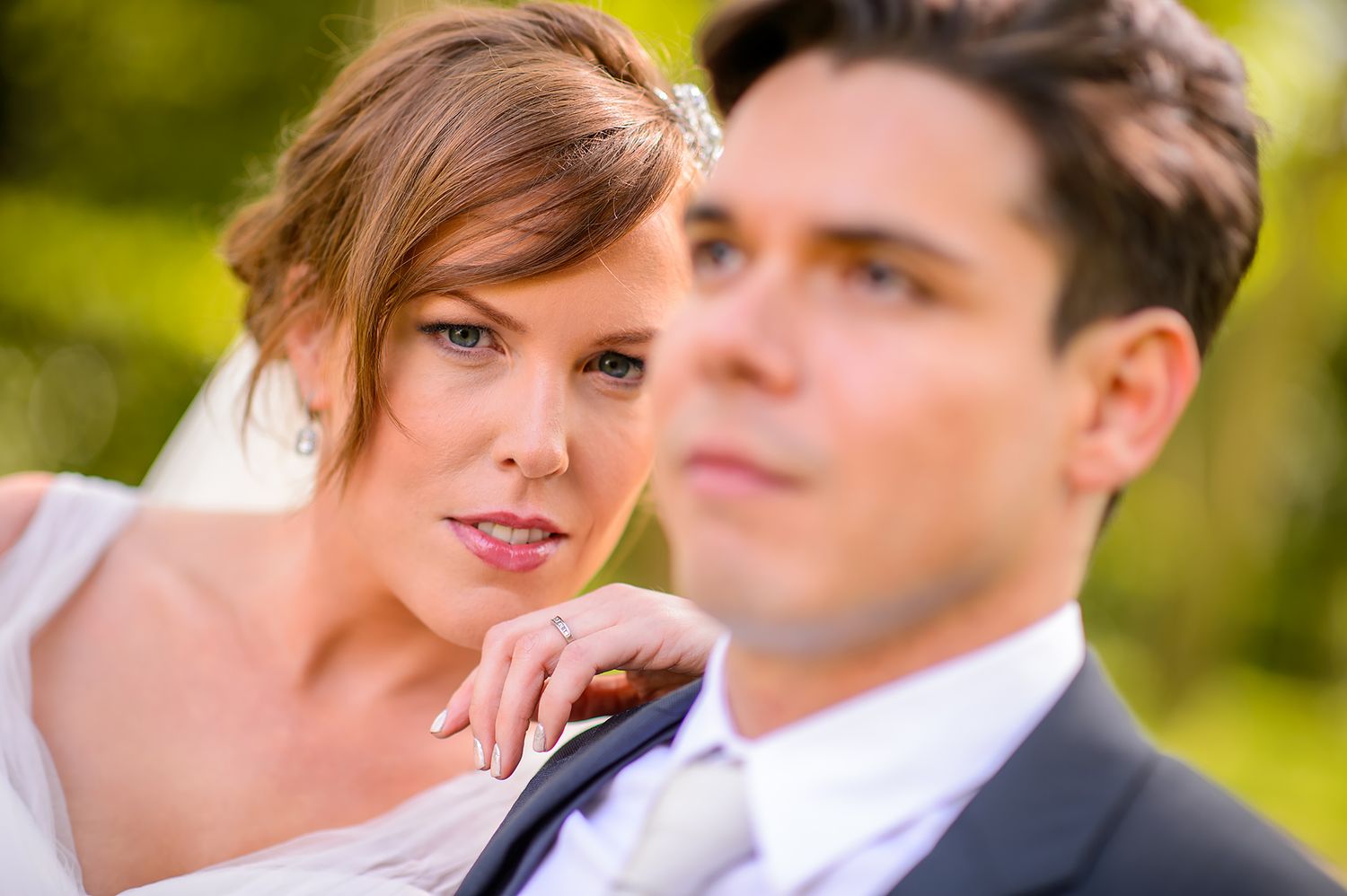 Two people share a tender moment on their wedding day in natural outdoor lighting.