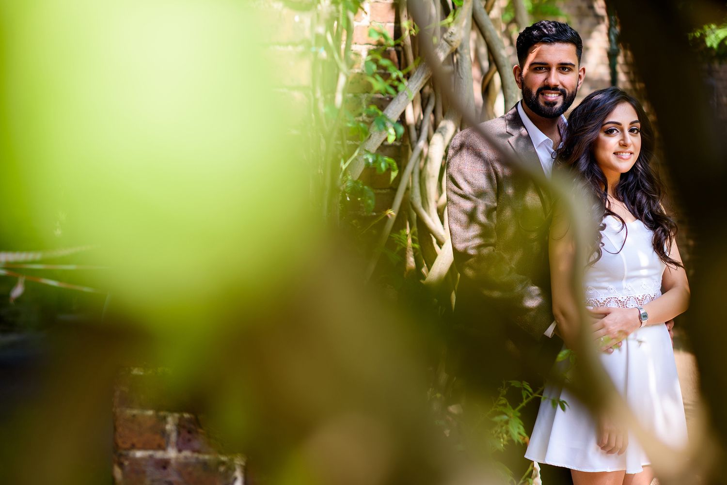 Intimate couple portrait through soft green foliage in natural lighting.