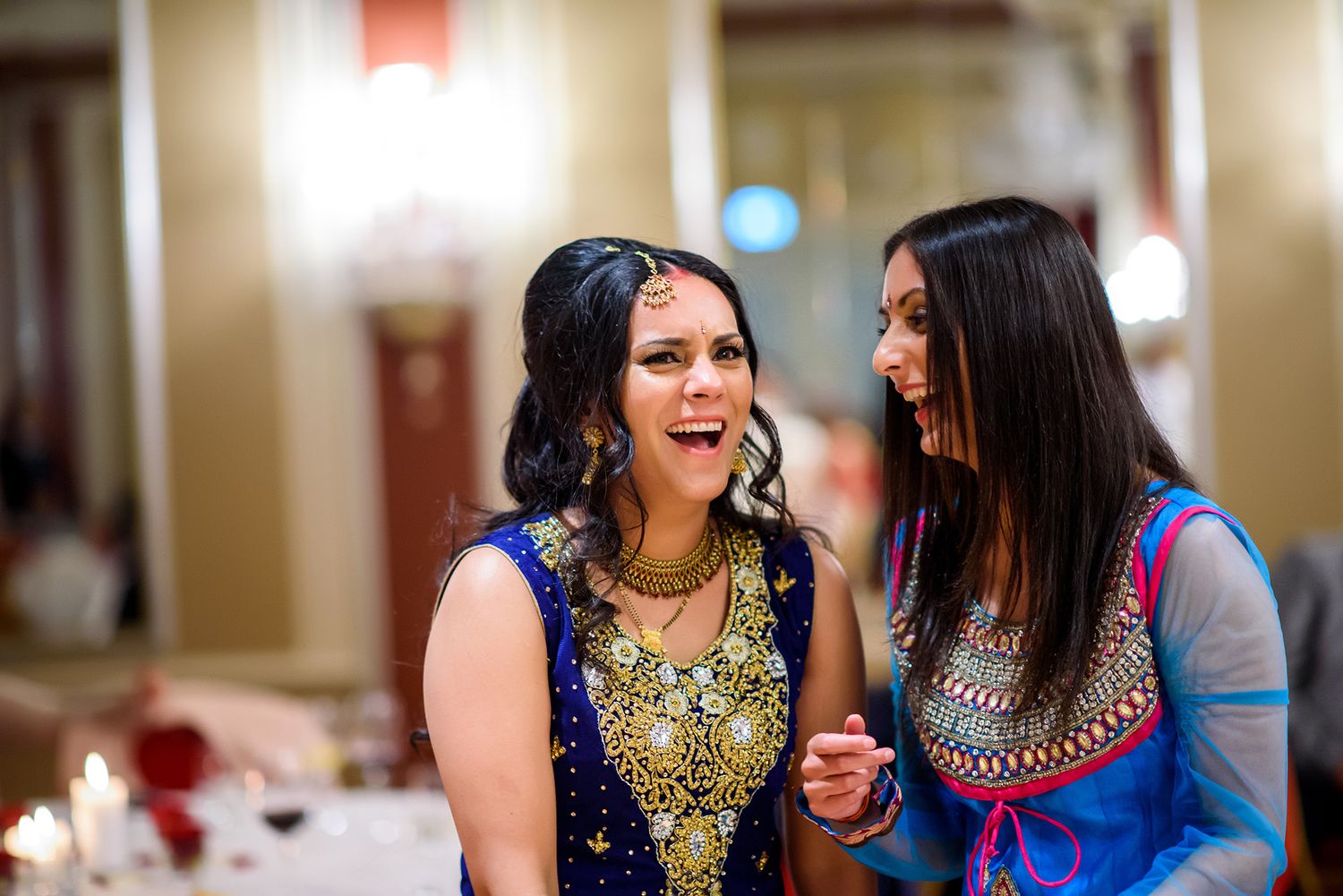 Joyful guests in traditional South Asian attire sharing laughter at formal celebration.