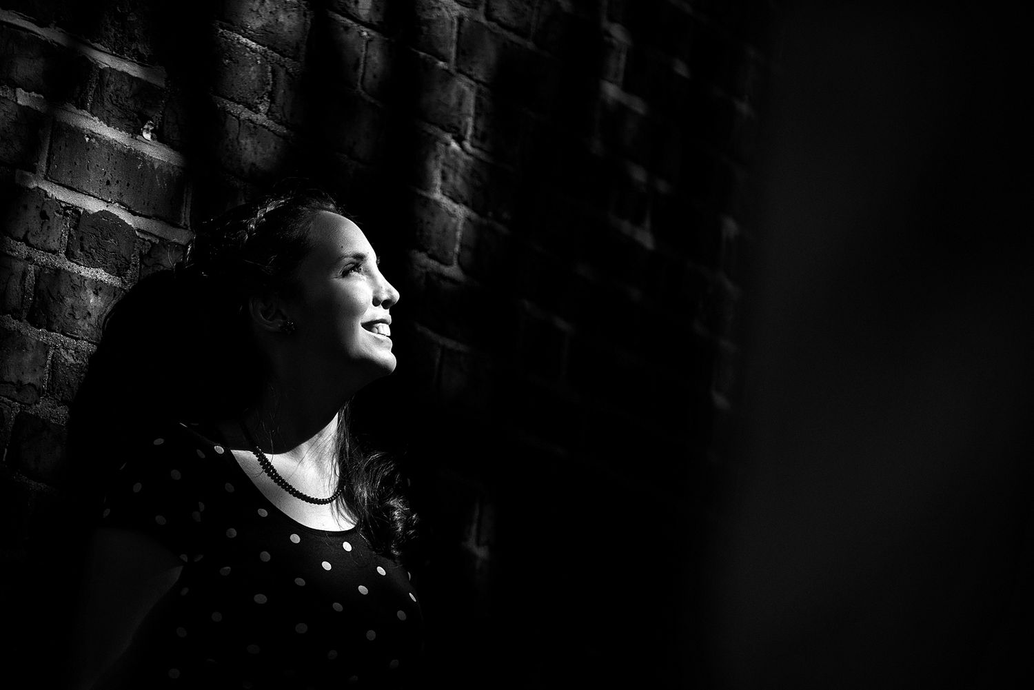 Dramatic side-lit black and white portrait against brick wall.