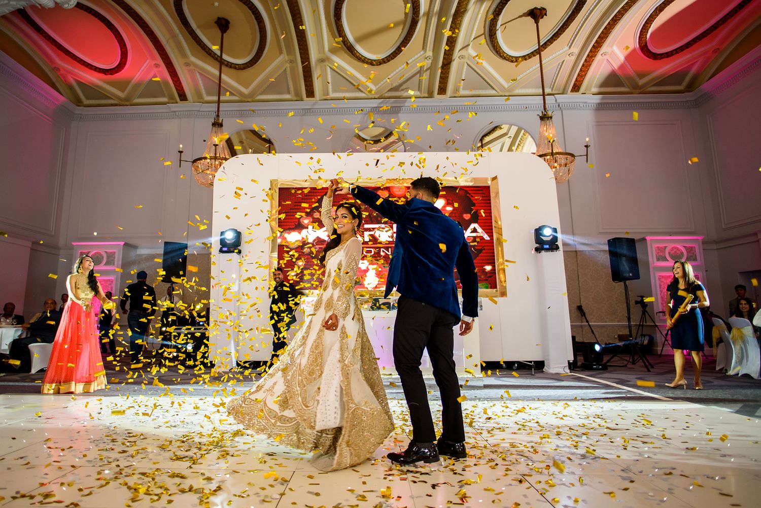 A crowd celebrates with confetti and dancing at an elegant wedding reception.