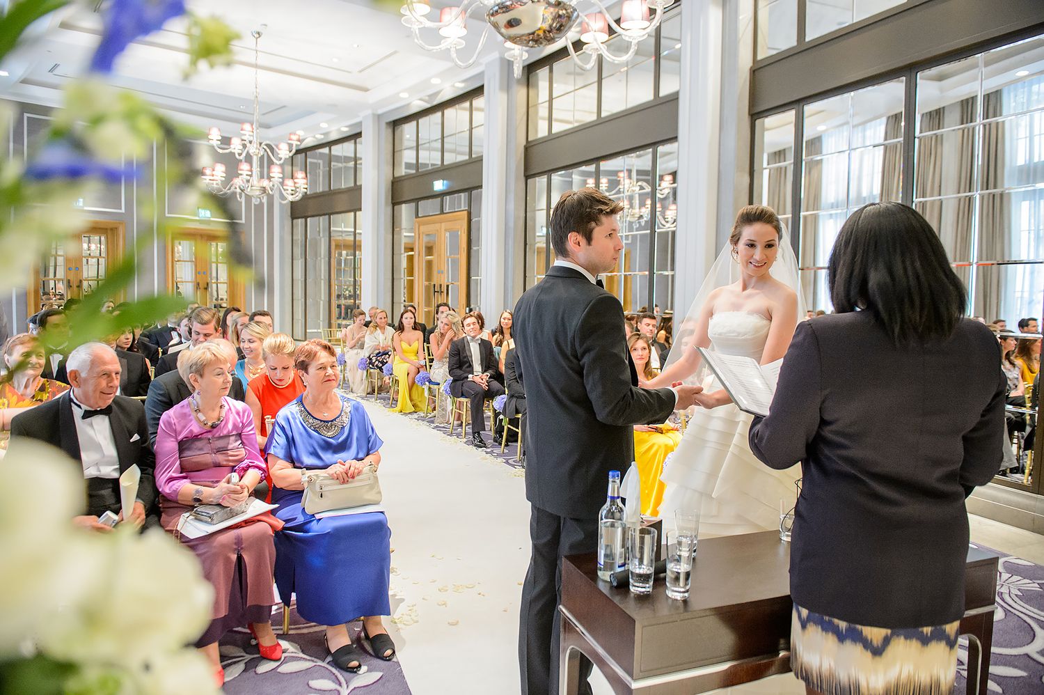 Bright ceremony space with chandelier and large windows during wedding proceedings.