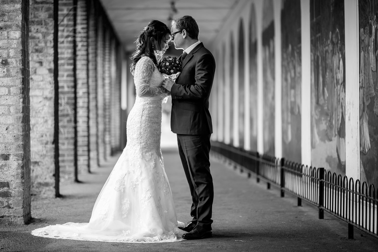 An elegant wedding portrait taken in a long brick colonnade hallway.