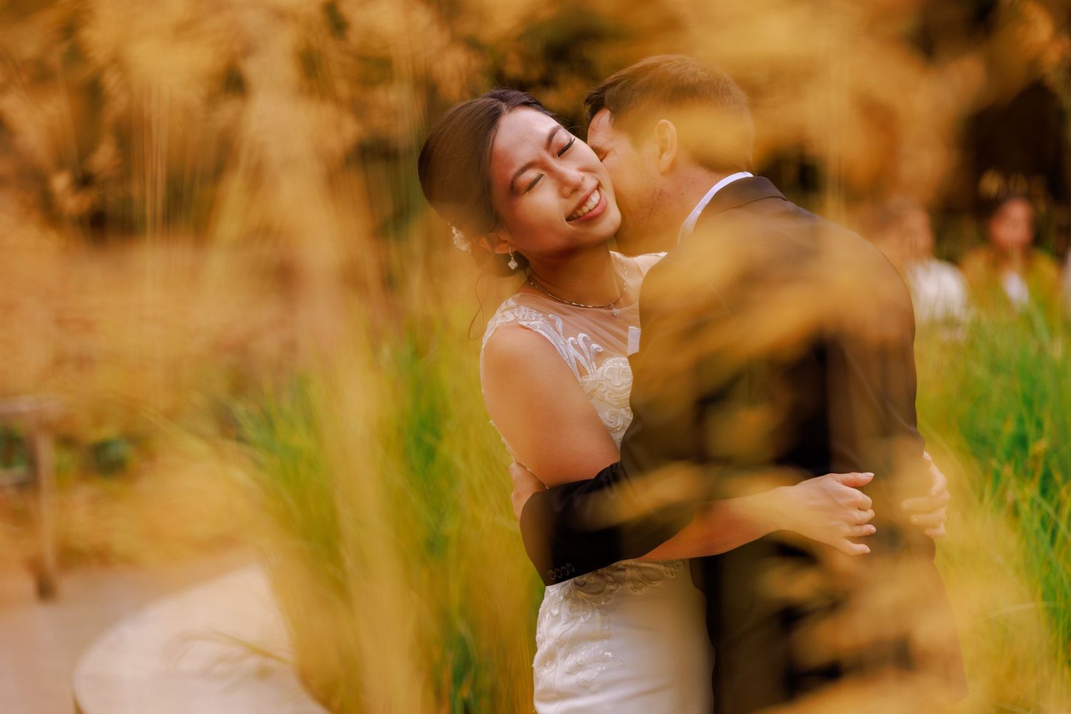 Romantic wedding couple portraits captured through golden wheat field during sunset.