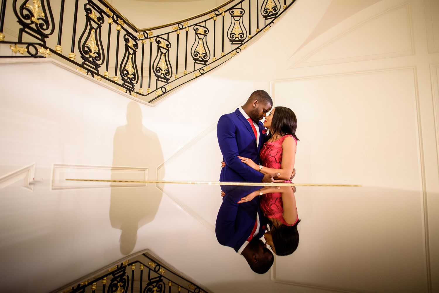 Couple interacting in a grand space with ornate iron railings and cream colored decor.