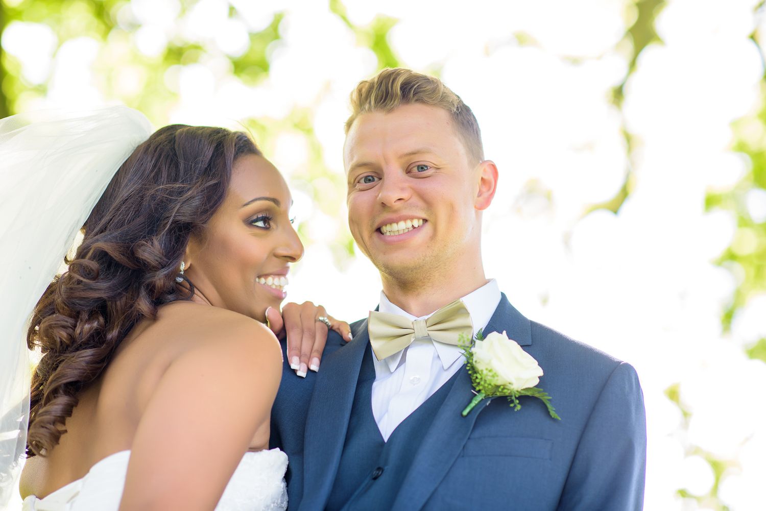 Wedding couple shares intimate moment under sunlit tree canopy.
