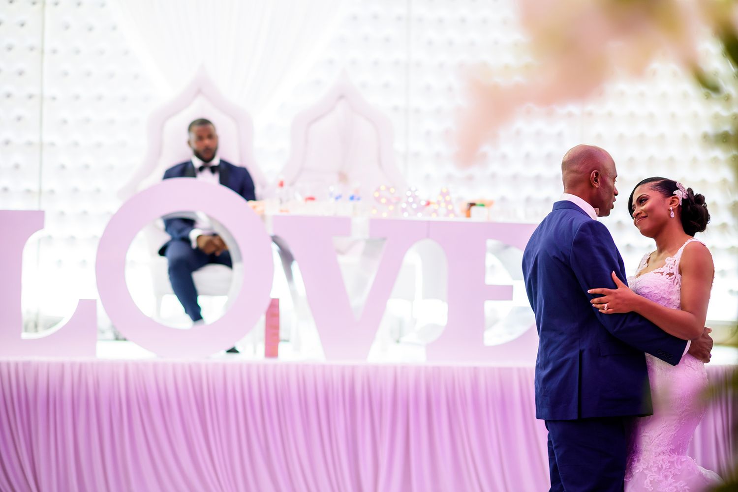 Newlyweds share their first dance under a pink LOVE sign at their wedding reception.